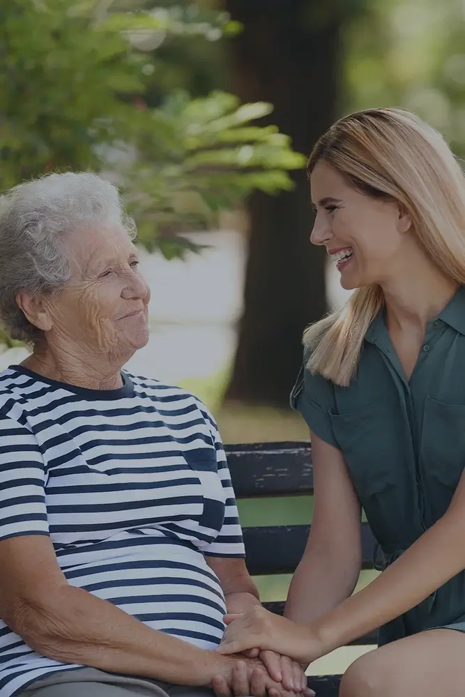 Smiling caregiver supporting elderly woman during a walk outdoors
